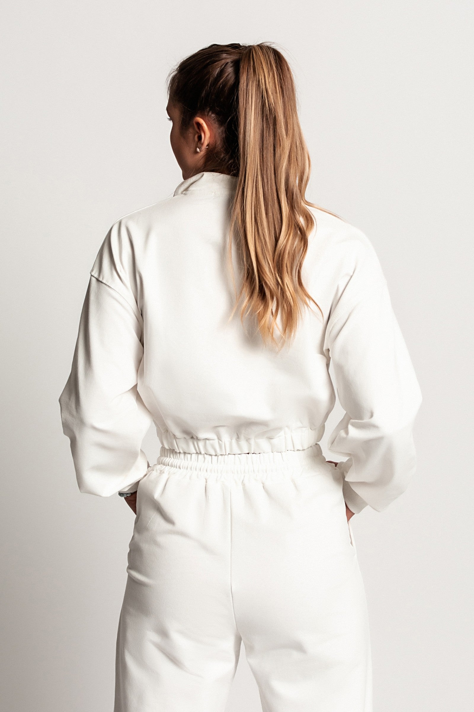 Bela skrajšana športna majica Polistena z dolgimi rokavi in visokim ovratnikom z zadrgo.